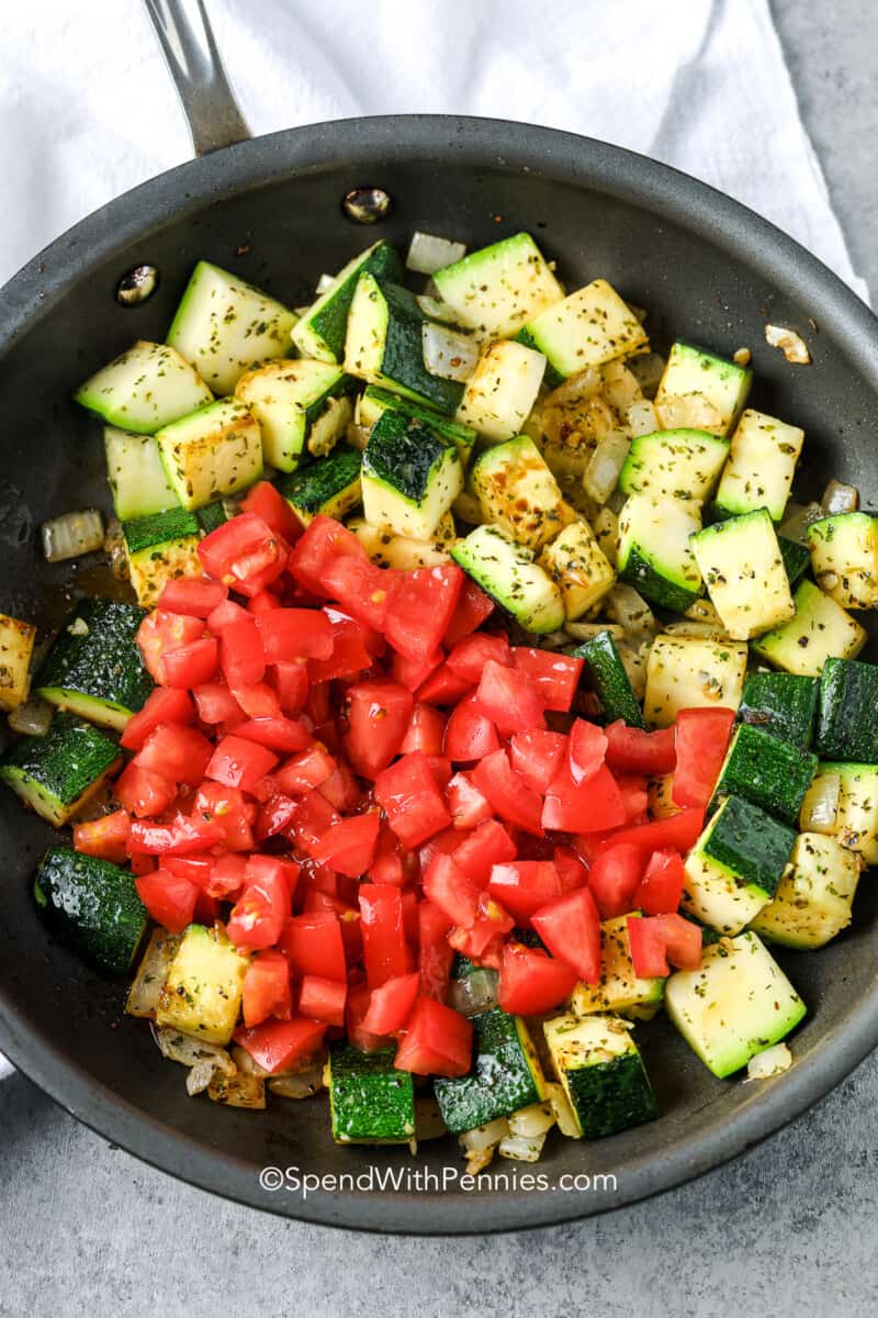 This zucchini and tomatoes recipe makes a savory side dish that everyone will love. The zucchini and tomatoes are lightly seasoned and then topped with melty cheese. This is so good served with pasta or some roasted chicken. #zucchiniandtomatoes #sauteedzucchini #zucchiniandtomatoesrecipe #spendwithpennies Sauteed zucchini, onions, and tomatoes in a pan