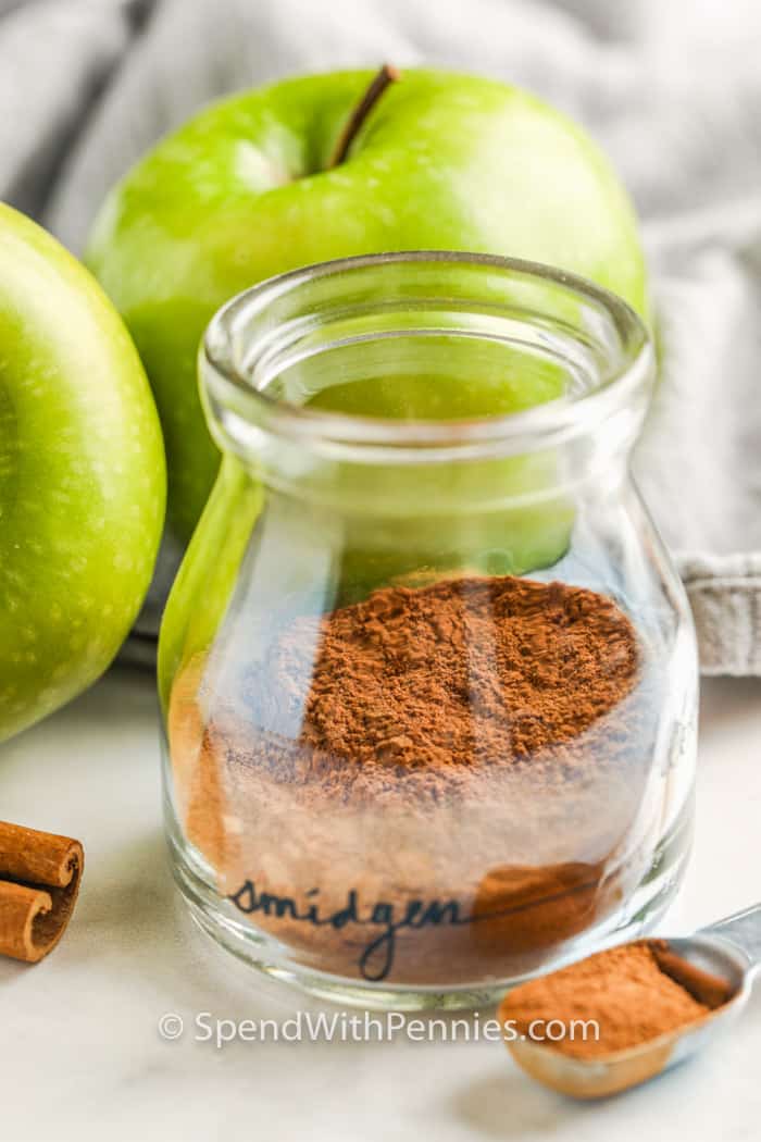 Apple Pie Spice in a jar with apples and cinnamon beside it