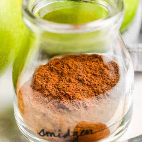 close up of Apple Pie Spice in a glass jar with apples in the back