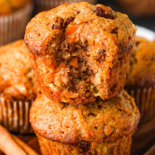 two Carrot Muffins stacked with one muffin with a bite taken out and a cinammon stick