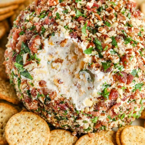 close up of Classic Cheese Ball with a bite taken out and crackers surrounding it on a plate
