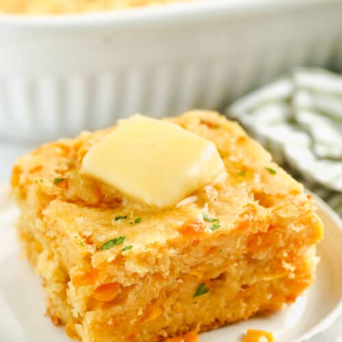 Cornbread Casserole on a white plate with butter and a casserole dish full in the back