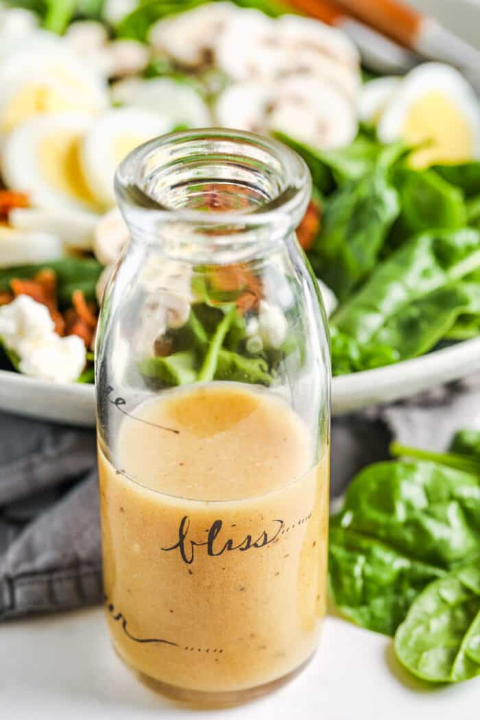jar of Spinach Salad Dressing with a bowl full of salad in the background