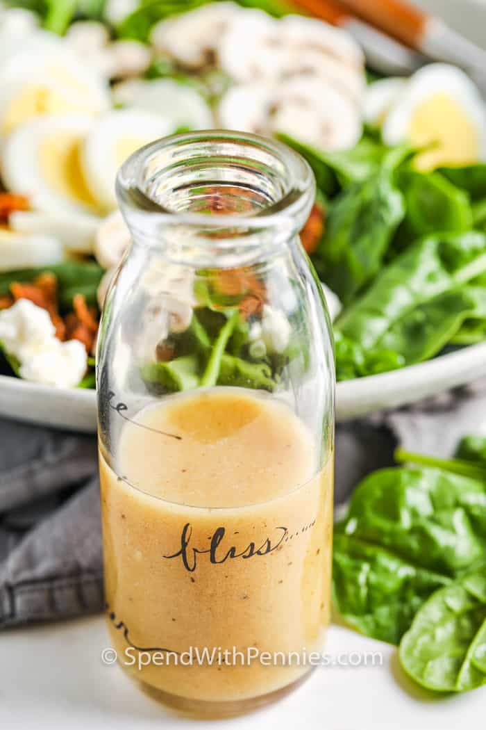 Spinach Salad Dressing in a jar with bowl of salad in the back