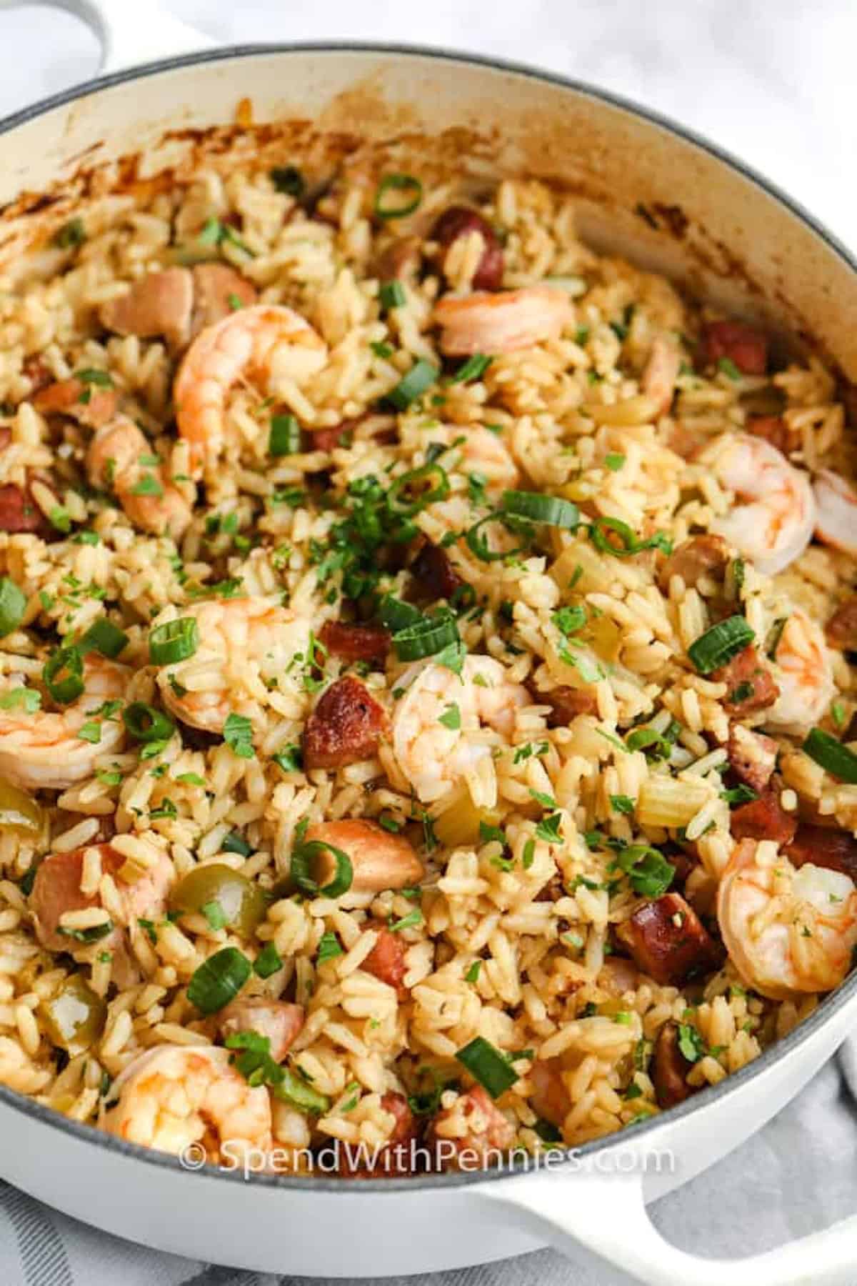 This Cajun jambalaya recipe is packed with smoky andouille sausage, tender chicken thighs, shrimp, vegetables, and Cajun-seasoned rice. It bakes in one oven-safe pot so the rice cooks evenly and soaks up all the savory broth. Serve it with warm French bread or cornbread for a cozy dinner that feels hearty, flavorful, and easy enough for a family meal. Pin this to your meal board. #spendwithpennies A pot of jambalaya.