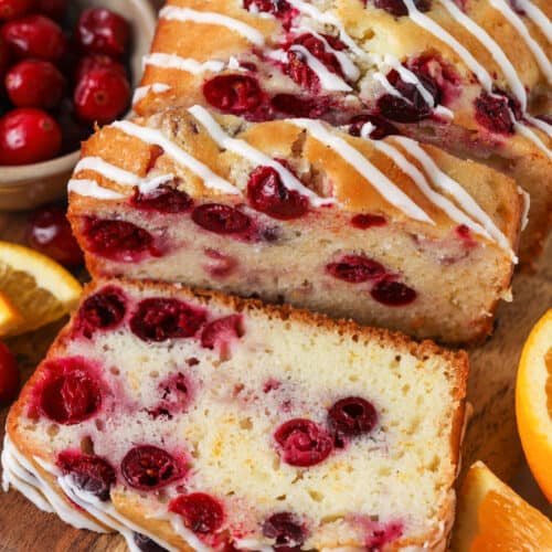 Cranberry Orange Loaf sliced with oranges and cranberries surrounding it