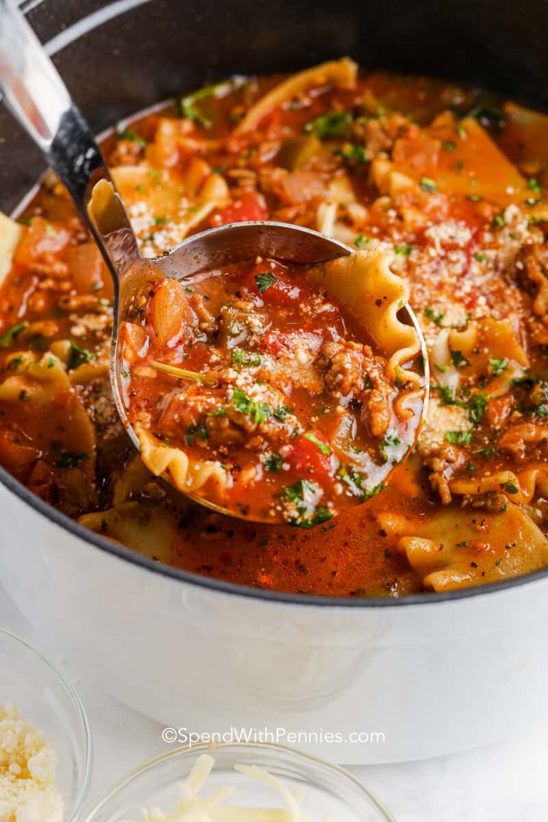 Everyone who loves Italian food will adore this tasty lasagna soup. Simple ingredients and easy prep make it the best soup for a weeknight or lunches all week long. Use instant lasagna noodles, Italian sausage, herbs, and spices cooked in a rich tomato broth. Switch sausage with chicken or turkey or make a vegetarian version with zucchini, kale, or extra spinach and mushrooms. Add some cheese on top for savory deliciousness. #lasagnasoup #recipeeasy #recipeonepot #spendwithpennies a ladle serving lasagna soup