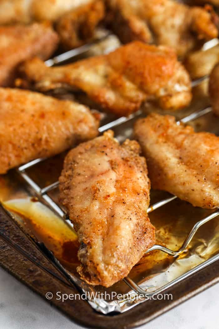 Crispy baked chicken wings are easy with simple ingredients and smart prep. Dry wings and rack baking help them cook evenly, while a quick uncovered chill helps the coating set. A special pantry staple gives the skin a crackly finish as it bakes. Cook until browned, then finish under the broiler for extra color. These wings pair well with any sauce, and reheating them on a rack brings back their crunch. #spendwithpennies Actually Crispy Oven Baked Wings cooked on a baking sheet