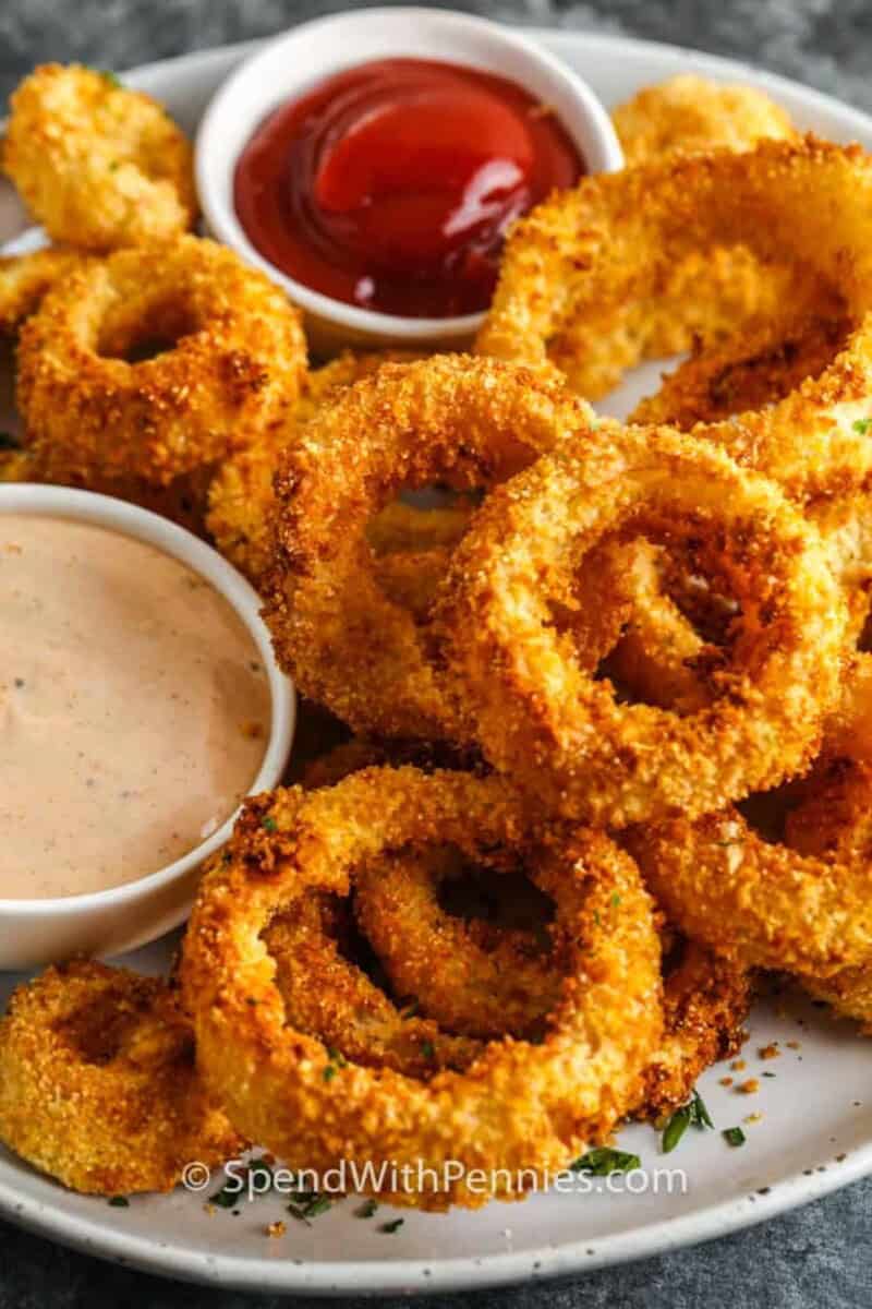Homemade air fryer onion rings can easily be made keto, paleo, or low carb, even vegan by switching out a few simple ingredients. Everyone can enjoy these delicious onion rings! #spendwithpennies #airfryeronionrings #onionrings #appetizer #sidedish #recipe #homemade #easy #batter #best #crispy a plate of onion rings.