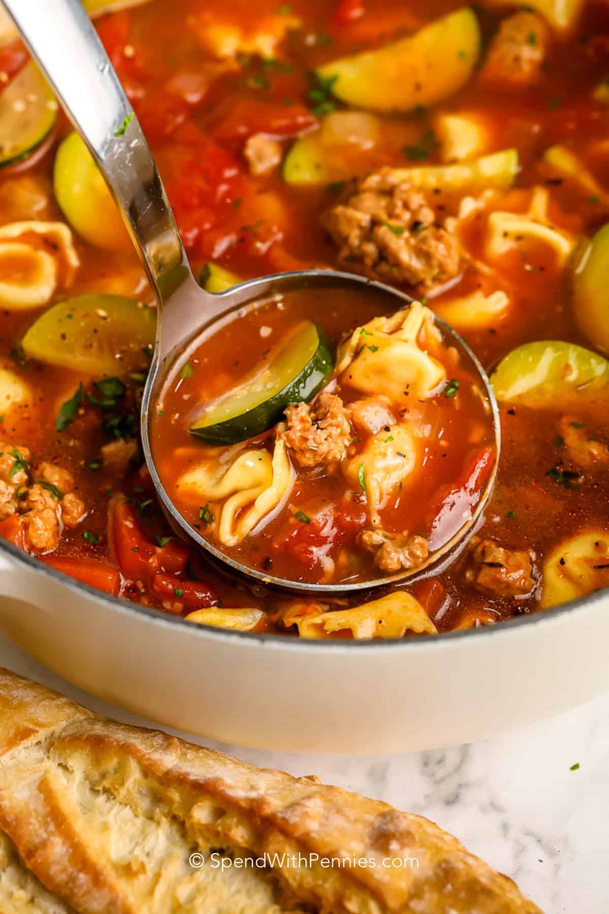 A ladle of cooked Sausage tortellini soup in a pot