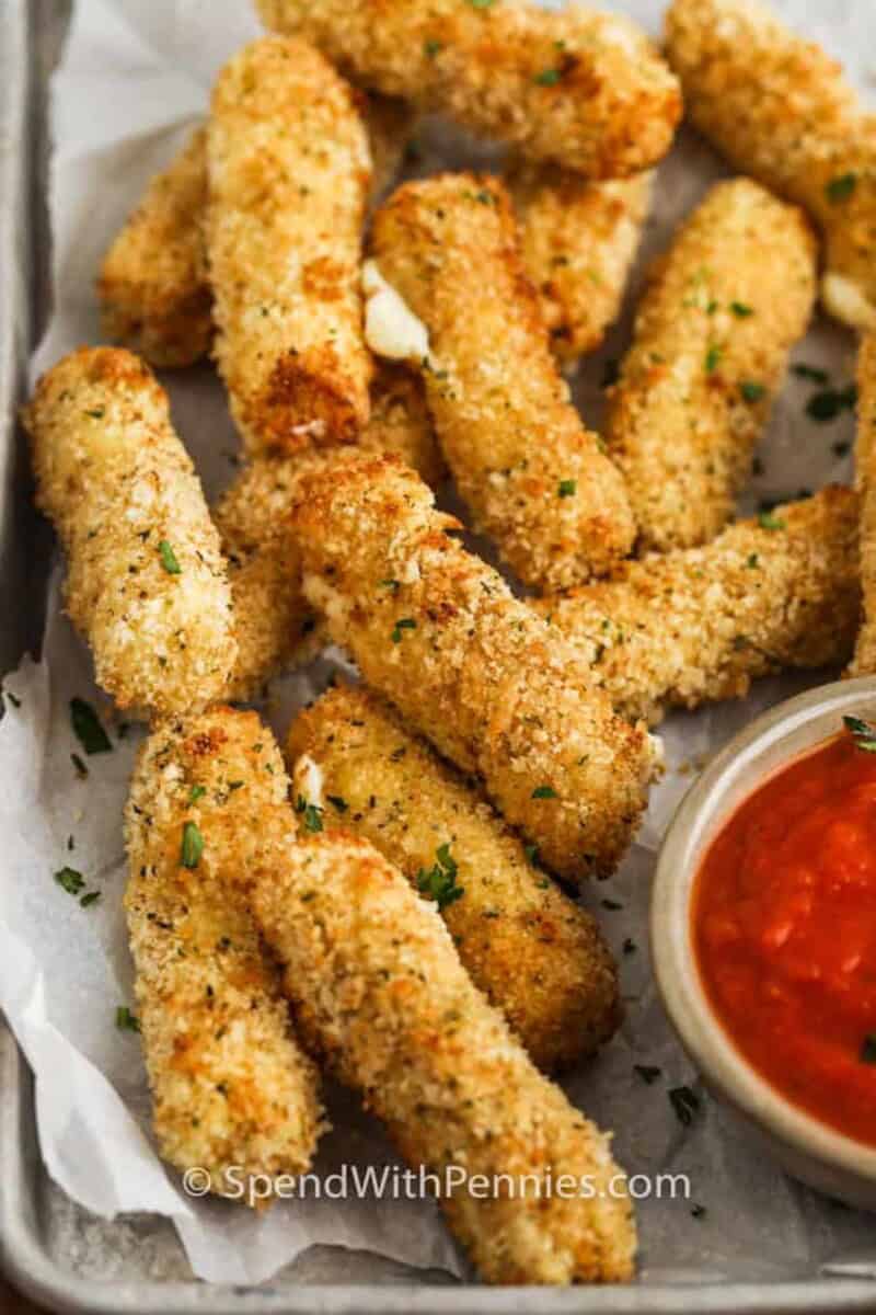 Air Fryer Mozzarella Sticks are quick and easy to make. We use panko breadcrumbs instead of wonton wrappers for the best flavor and crunch! #spendwithpennies #airfryermozzarellasticks #mozzarellasticks #appetizer #recipe #snack #homemade #frozen #best #panko #airfryer a plate of homemade air fryer mozzarella sticks with a side of marinara.