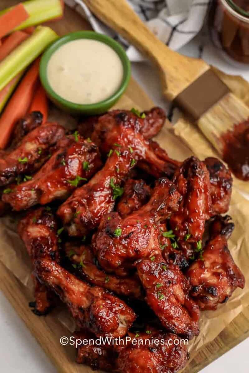 BBQ Chicken Wings taste amazing with ranch dressing or blue cheese. Try them with an array of dips and other party side dishes. #spendwithpennies #bbqchickenwings #chickenwings #appetizer #recipe #baked #crispy #easy #sauce #best #homemade #ovenbaked #ovenfried BBQ Chicken wings served with ranch dip and carrots and celery on a plate.