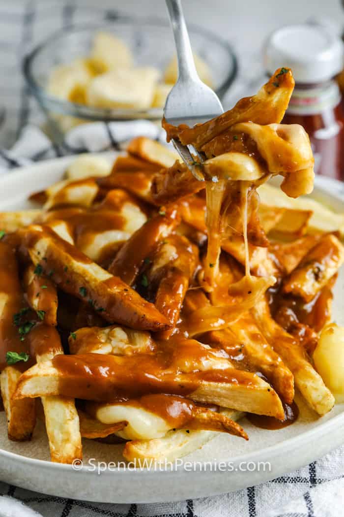 fork full of Poutine with plate full behind it