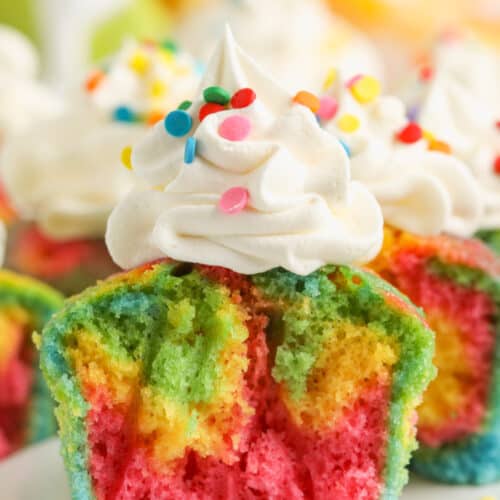 close up of Fun and Easy Rainbow Cupcakes with whipped cream topping