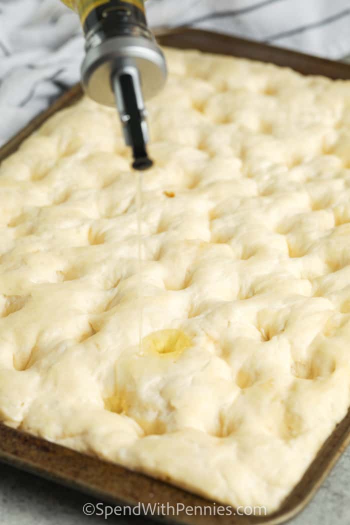 pouring olive oil over focaccia before baking