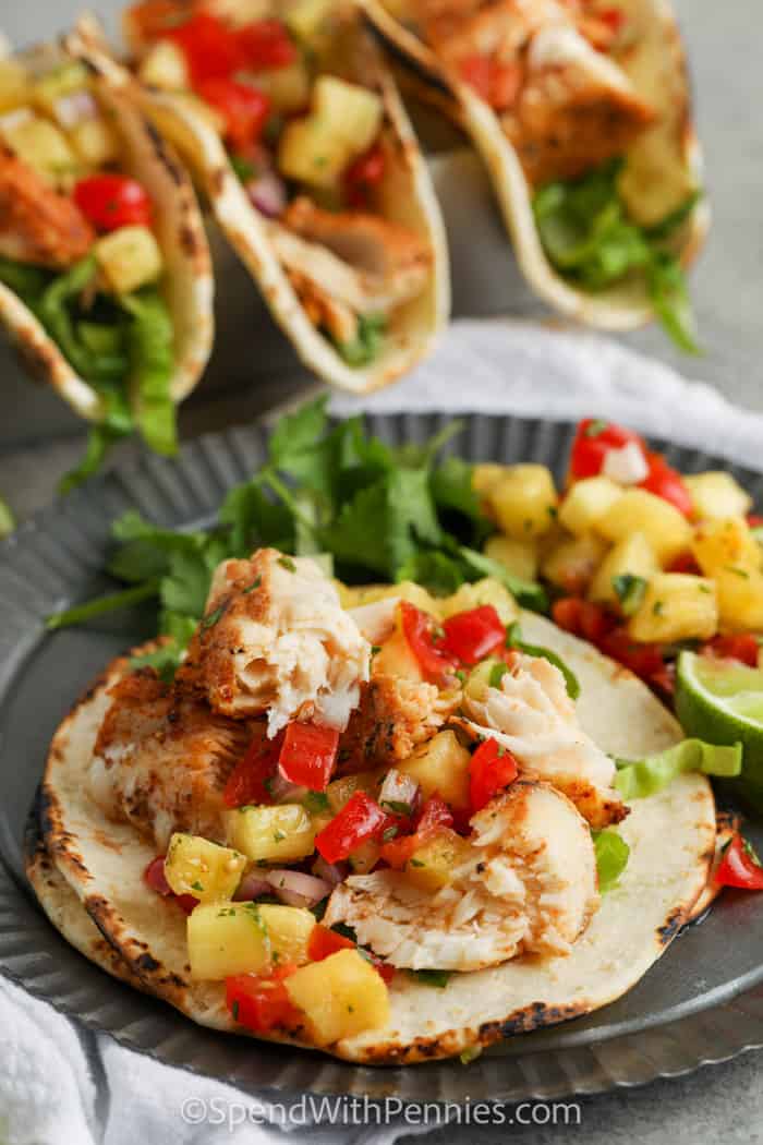 These Mahi Mahi Tacos are so easy to make, low in calories, but high in flavor. Blackened with different spices and a squeeze of lime, these fish tacos will be loved by all! #spendwithpennies open Mahi Mahi Tacos on a plate with tacos in the back