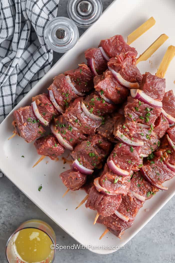 Garlic steak kabobs are a delicious mix of marinated steak and grilled onions, making them a tasty choice for outdoor parties and barbecues. The steak is tender and has a delightful garlic flavor, while the grill adds a smoky touch, creating kabobs that will satisfy your taste buds and leave you wanting more! #garlicsteakkabobs #steakkabobs #grilled #spendwithpennies raw steak on bamboo skewers