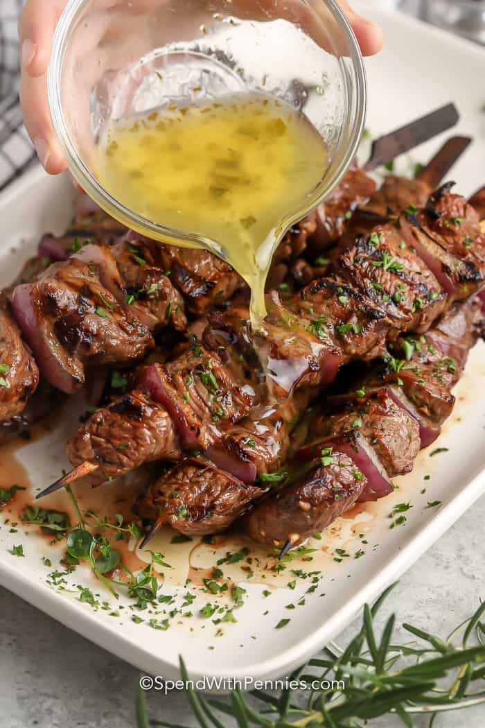 pouring garlic sauce over cooked steak kabobs