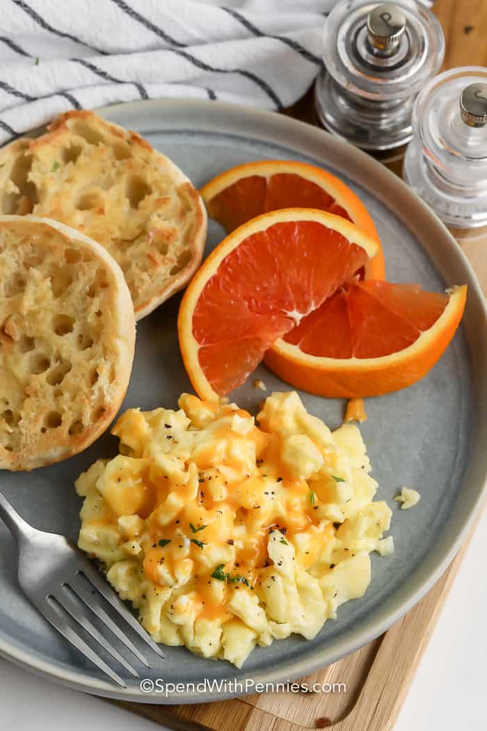 scrambled eggs on a plate with english muffins and orange wedges