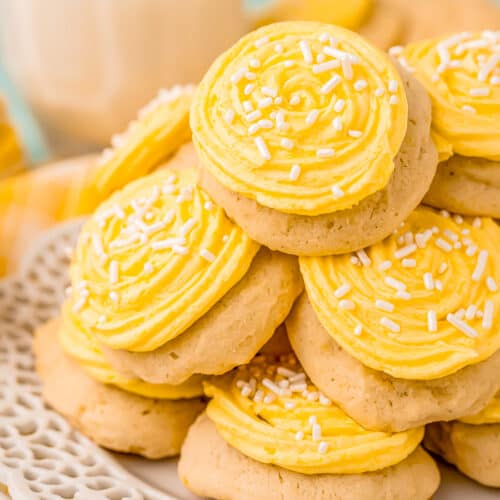 pile of lemon cookies with yellow icing and white sprinkles on a plate