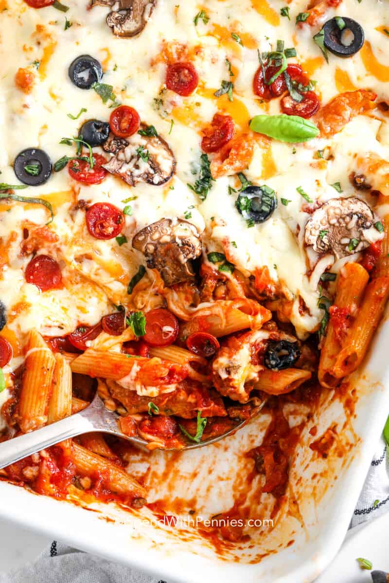 Pizza casserole is a deliciously easy alternative to a pizza or calzone with pasta instead of dough. Family meal? Potluck? Game night? Birthday party? Anything a pizza can do, this casserole can do too. It’s the perfect combination of a supreme pizza and a cheese-loaded casserole layered with pasta. Pizza casserole is a deliciously easy alternative to a pizza or calzone with pasta instead of dough. #pizzacasserole #supremepizzacasserolerecipe #supremepizza #spendwithpennies a serving spoon in a baked supreme pizza casserole