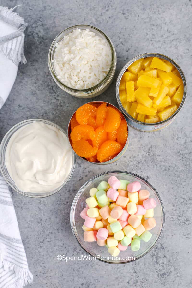 Thanksgiving dinner tables (or any Holiday Meal) wouldn't be complete without Ambrosia Salad. Also known as 5-Cup salad, it contains coconut, pineapple, and oranges but we add other goodies from time to time including maraschino cherries, walnuts, fruit cocktail, and/or pecans! #ambrosiasalad #dessert #sidedish #spendwithpennies ingredients for ambrosia salad on the counter