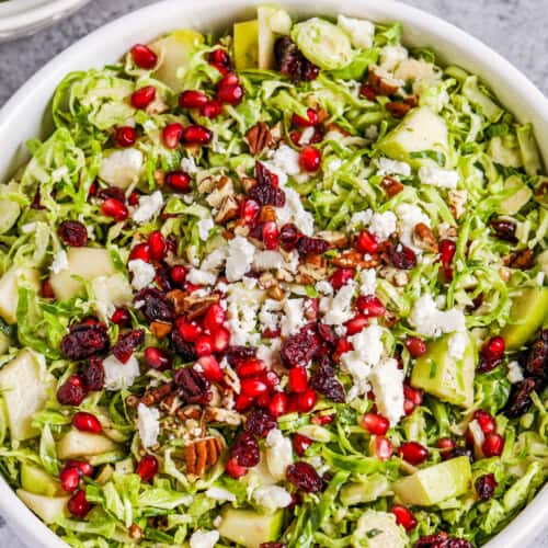 Brussels sprout salad in a white bowl topped with feta and pomegranate