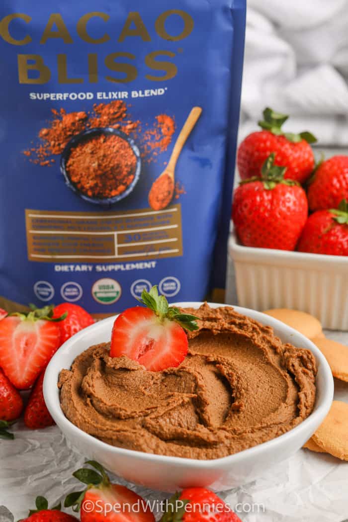 Chocolate Hummus in a bowl with strawberries and cacao bliss in the background