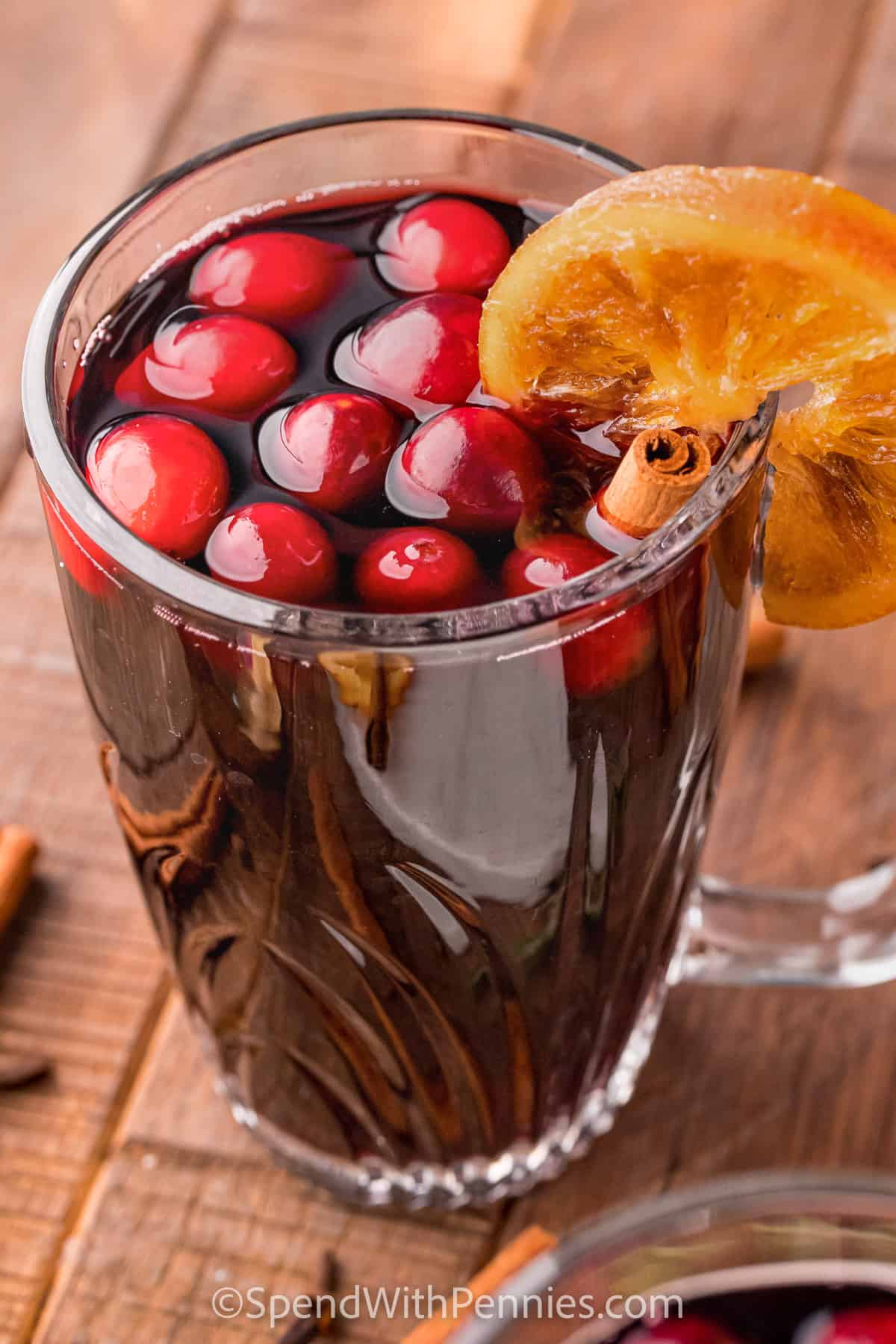 Make the holidays special this year with a sweet and savory mulled wine recipe! Why not serve this heart-warming beverage at the next Christmas party? Keep a small bowl of star anise, allspice berries, cinnamon sticks, rosemary sprigs, and candied orange peels close by so guests can garnish their own cups of mulled wine! Everyone will enjoy making their own signature drink! #spendwithpennies #mulledwine #recipe #christmas close up of Mulled Wine in a glass