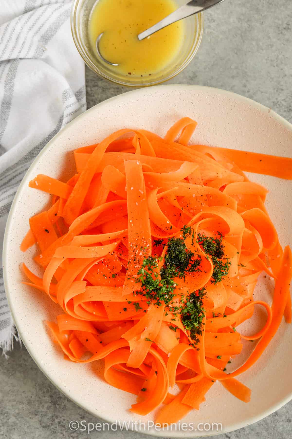Carrot salad is a fresh and vibrant dish that’s light yet so flavorful. Grated or ribboned carrots are tossed with a tangy mix of lemon, honey, and Dijon for a simple dressing that makes them shine. Dill and parsley add an herb note that brings out the zesty taste in every bite. Served cold, it’s refreshing, easy, and the perfect side dish to make for family meals or summer dinners. #spendwithpennies Carrot Salad being prepared