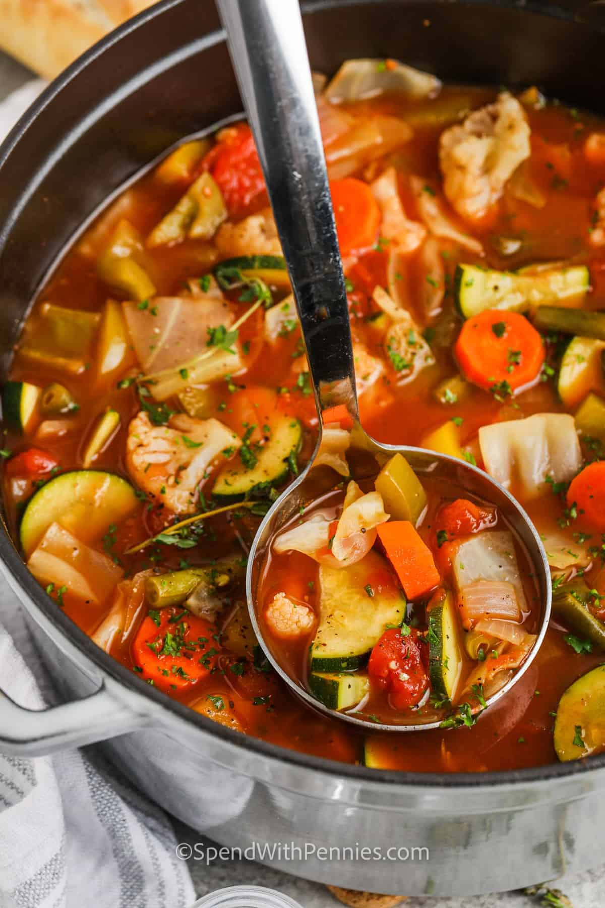 This homemade vegetable soup is super tasty and good for you! It's made with cabbage and lots of healthy veggies in a beef broth, making it a winner. You can also add pre-cooked shredded chicken or leftover beef. If you like, toss in some barley or a yummy soup mix for extra flavor. It's simple to make and oh-so-delicious, the perfect cozy soup! #vegetablesoup #homemade #soup #spendwithpennies Vegetable Soup in a pot with a ladle