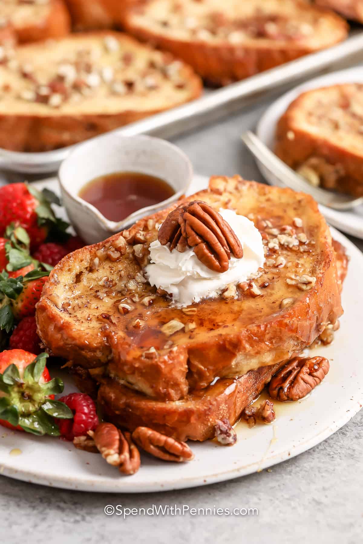 Two slices of overnight french toast being served topped with whipped cream and pecans