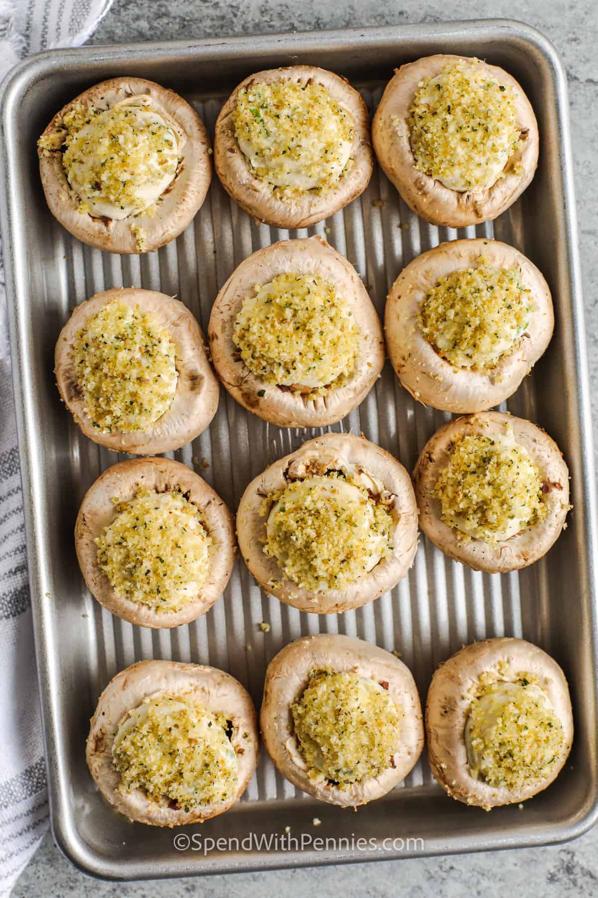 Impress your party guests with these homemade stuffed mushrooms! Whip up this tasty recipe easily by stuffing small white mushrooms with a blend of cream cheese and spices. Sprinkle breadcrumbs and parmesan on top, bake until golden, and a delicious appetizer is ready to enjoy! #stuffedmushrooms #easystuffedmushrooms #appetizer #spendwithpennies cooked Stuffed Mushrooms on a baking sheet