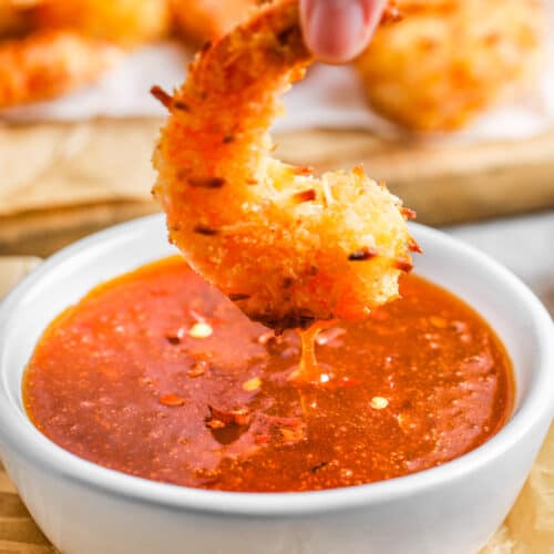 A breaded shrimp being dipped in a bowl of sweet chili sauce