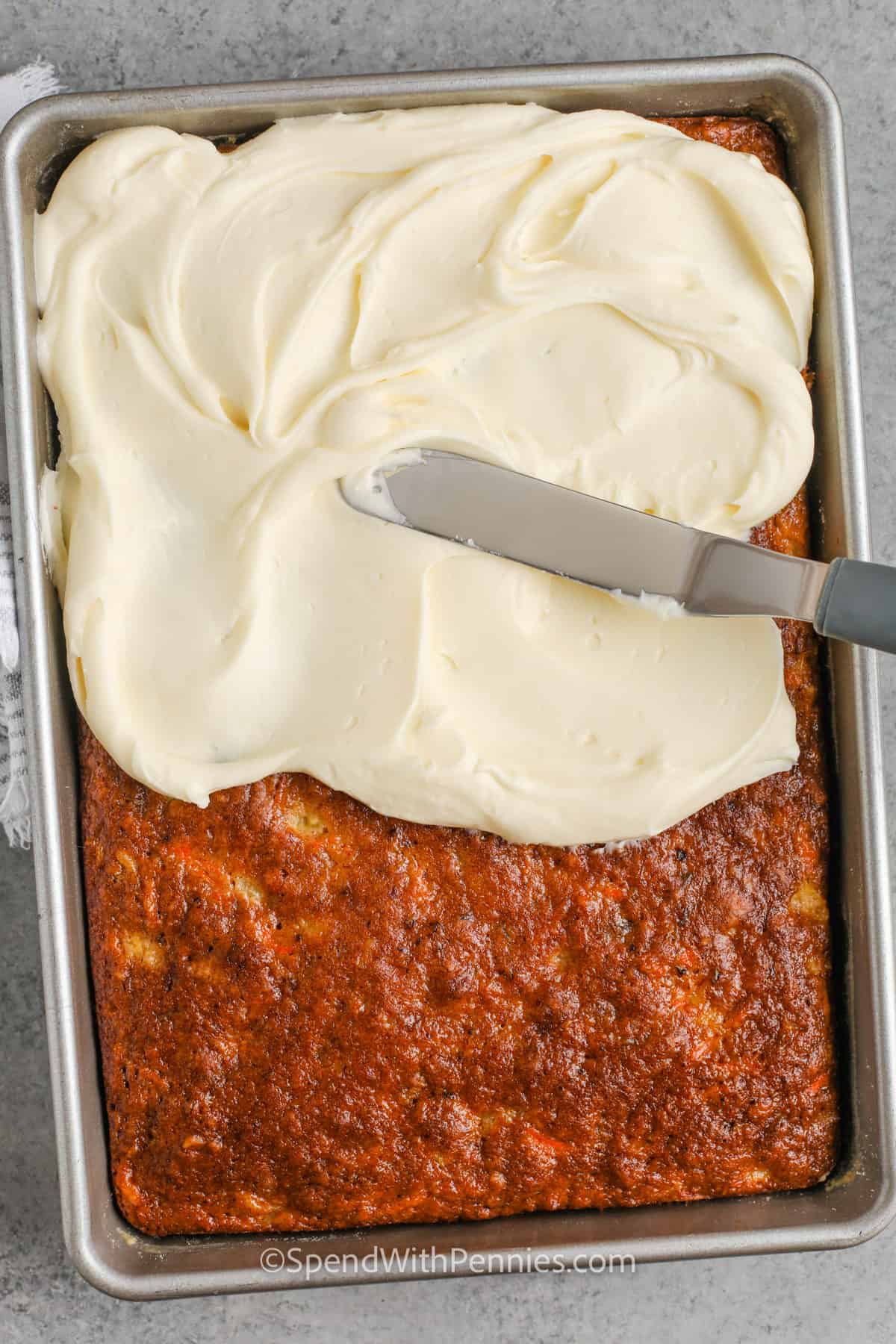 This is simply the best carrot cake for dessert. The family will ask for this carrot cake time and time again. With so many flavorful ingredients like pineapple, walnuts, coconut, and raisins it sure beats the typical spiced carrot cake. With a final cream cheese frosting, it just might become a weekly favorite. #thebestcarrotcake #carrotcakerecipe #carrotcake #spendwithpennies Cream Cheese icing being spread on carrot cake
