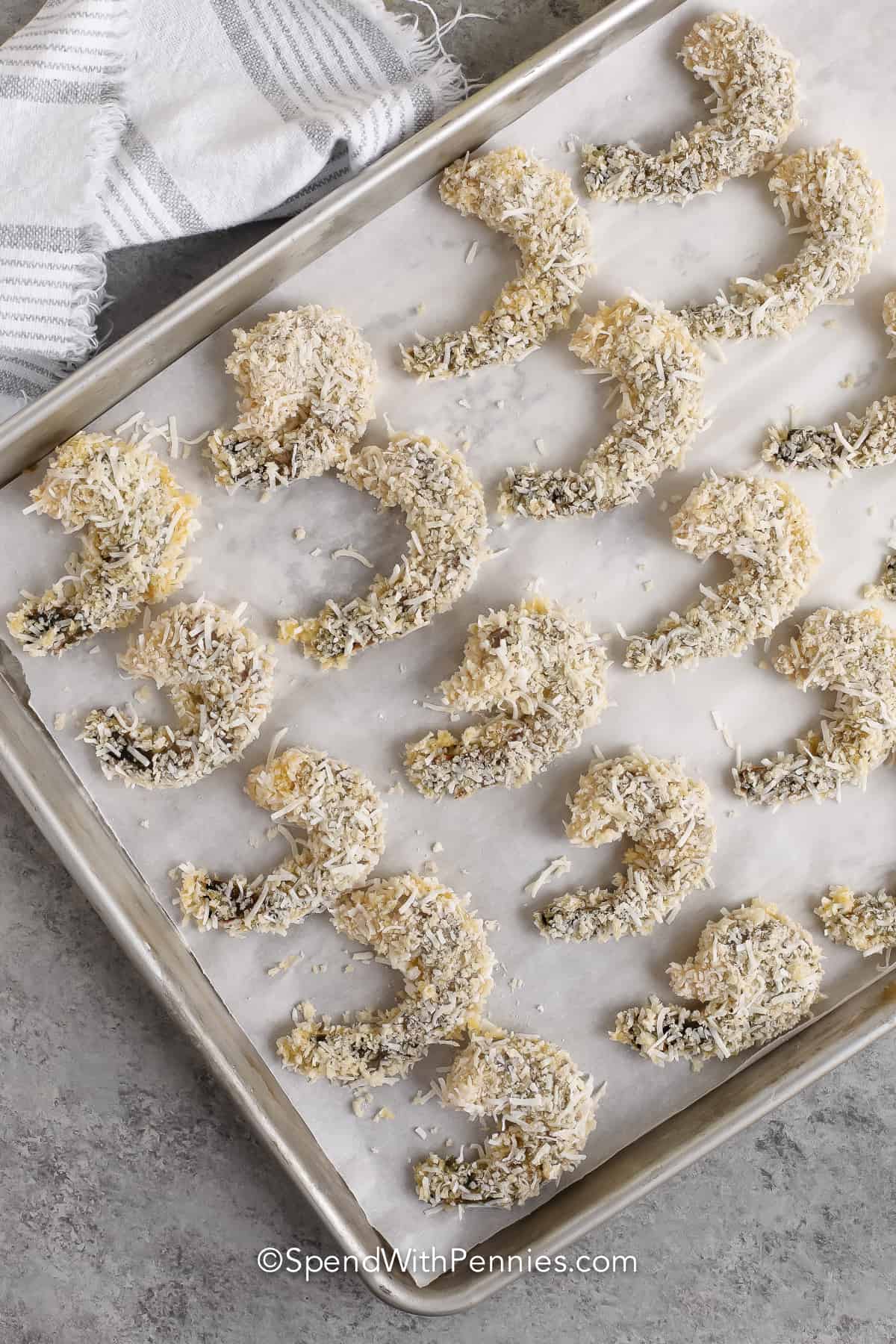 breaded coconut shrimp prepared to be baked on a parchment lined baking tray