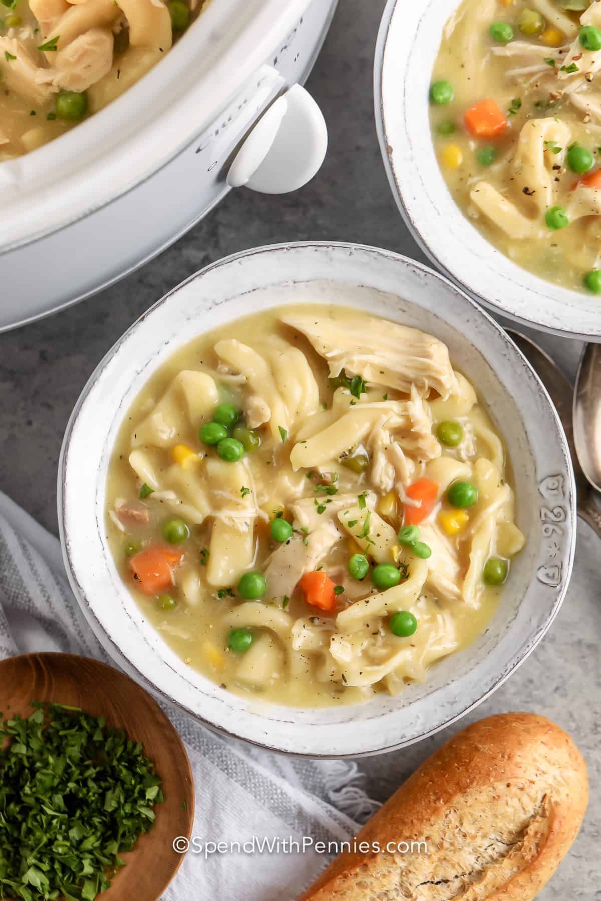 Crockpot chicken and noodles is so creamy, the whole family will love it. Make this soup when the wind is knocking at the door, or when something creamy and comforting is needed for dinner. It is so easy and simple to make this delicious soup. #crockpotchickenandnoodles #chickenandnoodlesinthecrockpot #chickennoodlesoup #spendwithpennies bowl of Crock Pot Chicken and Noodles with bread