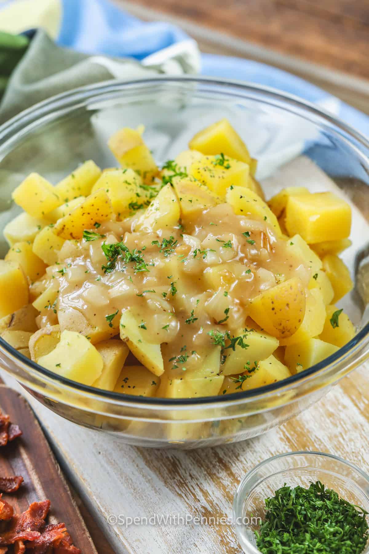 Everyone will love this authentic german potato salad. Try a new style of potato salad made with a tangy vinaigrette. This salad is made with red or yellow potatoes, vinegar, bacon bits, and some celery. Serve it warm or cold, either way and it will still get rave reviews! #germanpotatosalad #germanpotatosaladrecipe #coldgermanpotatosalad #spendwithpennies adding dressing to potatoes to make German Potato Salad