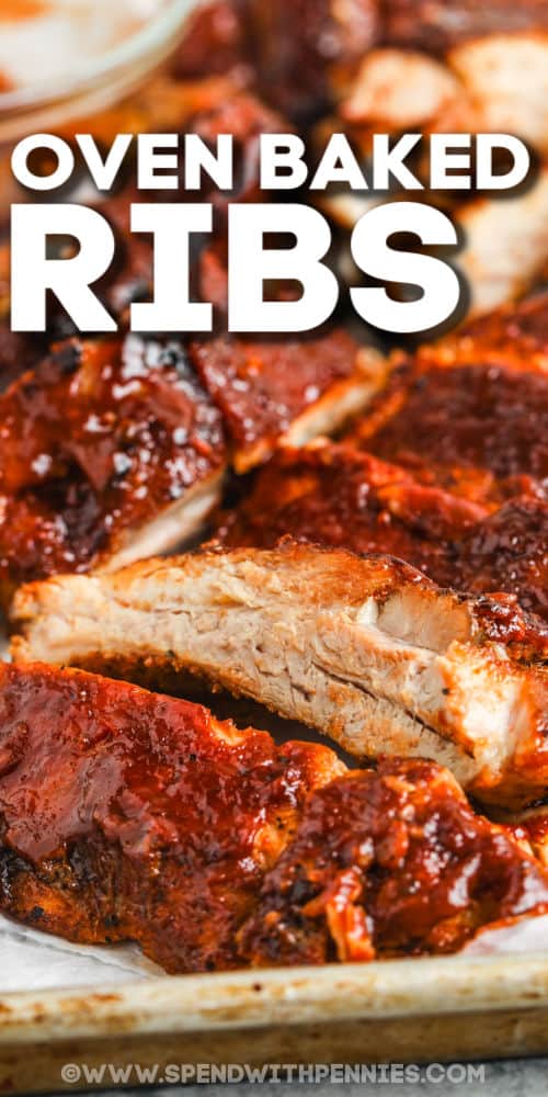Ribs in the oven are so juicy and tender that they fall right off the bone. Seasoned with a homemade rib rub and smothered in your fave BBQ sauce, this easy rib recipe is easy to enjoy all year round! Serve with a side of baked beans and fresh salad for a meal everyone will love! #spendwithpennies #ovenbaked #barbecueribs #grilling close up of Oven Baked Ribs slices with writing