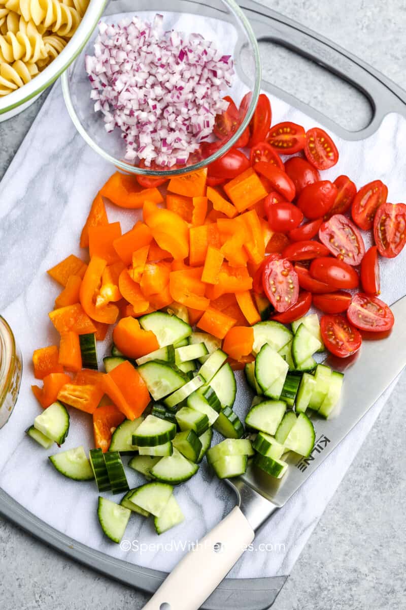 Make this creamy pasta salad recipe as a stand-alone healthy meal, or as a take-along for a family picnic. Made with Italian dressing, it's so versatile! Add some bacon, chicken, shrimp, or tuna as added protein. #spendwithpennies #pastasaladrecipe #recipe #pastasalad Ingredients for an easy pasta salad on a cutting board