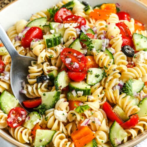 close up of an easy pasta salad in a white serving bowl with a serving spoon