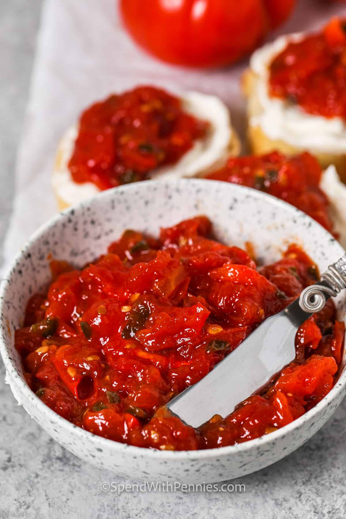 This sweet and spicy tomato jam is so simple and easy to toss together. Tomatoes are simmered with a little honey, some serrano chilis, and some apple cider vinegar. It is the best for topping sandwiches and adding to omelets. So simple, so easy, and so tasty. #tomatojamrecipe #homemadetomatojam #easytomatojam #spendwithpennies bowl of Tomato Jam