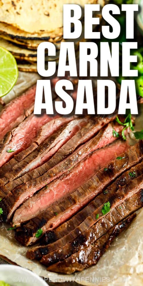 Carne Asada is a tasty Mexican-inspired steak recipe. Flank steak (or skirt steak) is marinated in an easy citrus garlic marinade and grilled to juicy perfection! Top with pico de Gallo, fresh guacamole, and your favorite veggies. #spendwithpennies #carneasada #maindish #tacos Carne Asada Recipe plated with limes and tortillas in the background with writing