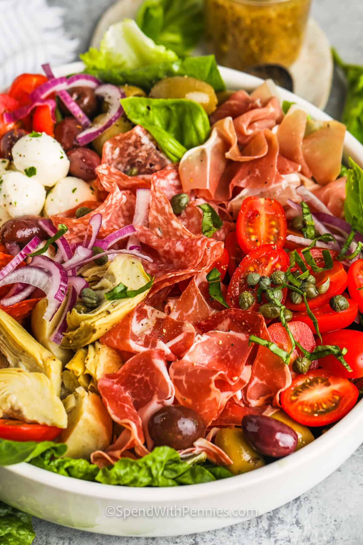 Make a simple and easy antipasto salad that everyone will enjoy. This salad is made with easy-to-find ingredients like tomatoes, romaine, bocconcini cheese, red onion, and an Italian dressing. Don't forget the salami and prosciutto. Sometimes the best side dishes are the ones that are simple and easy to make! #antipastosalad #easyrecipe #healthyrecipe #spendwithpennies close up of bowl of Antipasto Salad