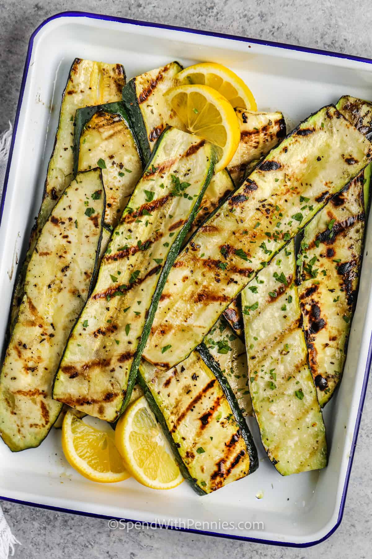 In this grilled zucchini recipe, tender and crispy zucchini are made on the grill. Low in calories and low in carbs, there is so much to love about the zucchini in this recipe. Chop, season, skewer, and cook, that's it! It is so easy to vary this recipe by adding some eggplant, cheese, or tomatoes to the skewer. #grilledzucchini #grilledzucchinirecipe #zucchinigrilled #spendwithpennies Grilled zucchini with lemon wedges in a dish