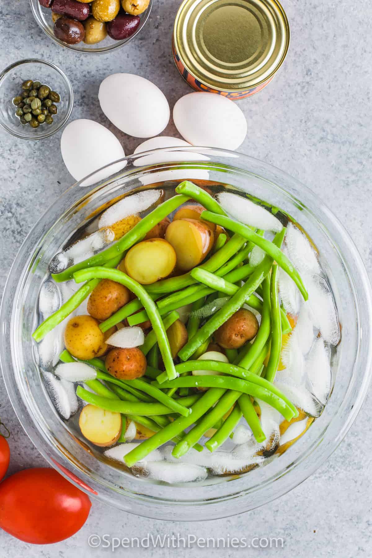 This Nicoise salad is a flavorful and protein-packed salad that everyone will enjoy. The ingredients in this French salad stray a little bit from the ordinary making it packed full of flavor. Included are fish like salmon, or tuna, potatoes, lettuce, capers, olives, and more, which are tossed in a tangy vinaigrette. #nicoisesalad #saladenicoise #nicoisesaladrecipe #spendwithpennies washing potatoes and beans in an ice bath to make Nicoise Salad