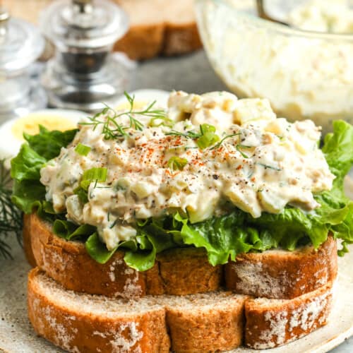 close up of a Tuna Egg Salad sandwich on a plate with bowl full of salad in the back