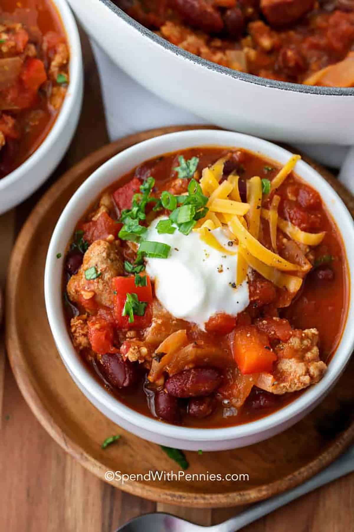 This easy turkey chili recipe is the ultimate comfort food. Ground turkey is a healthy low-fat alternative to ground beef. Add in some kidney beans, tomato sauce, and seasoning and the final result is a hearty chili that the whole family will love. Cook it in the crock pot, or on the stove. Either way, it will make a delicious bowl of chili. #turkeychili #turkeychilirecipe #chiliwithturkey #spendwithpennies Turkey Chili with sour cream , green onions and cheese