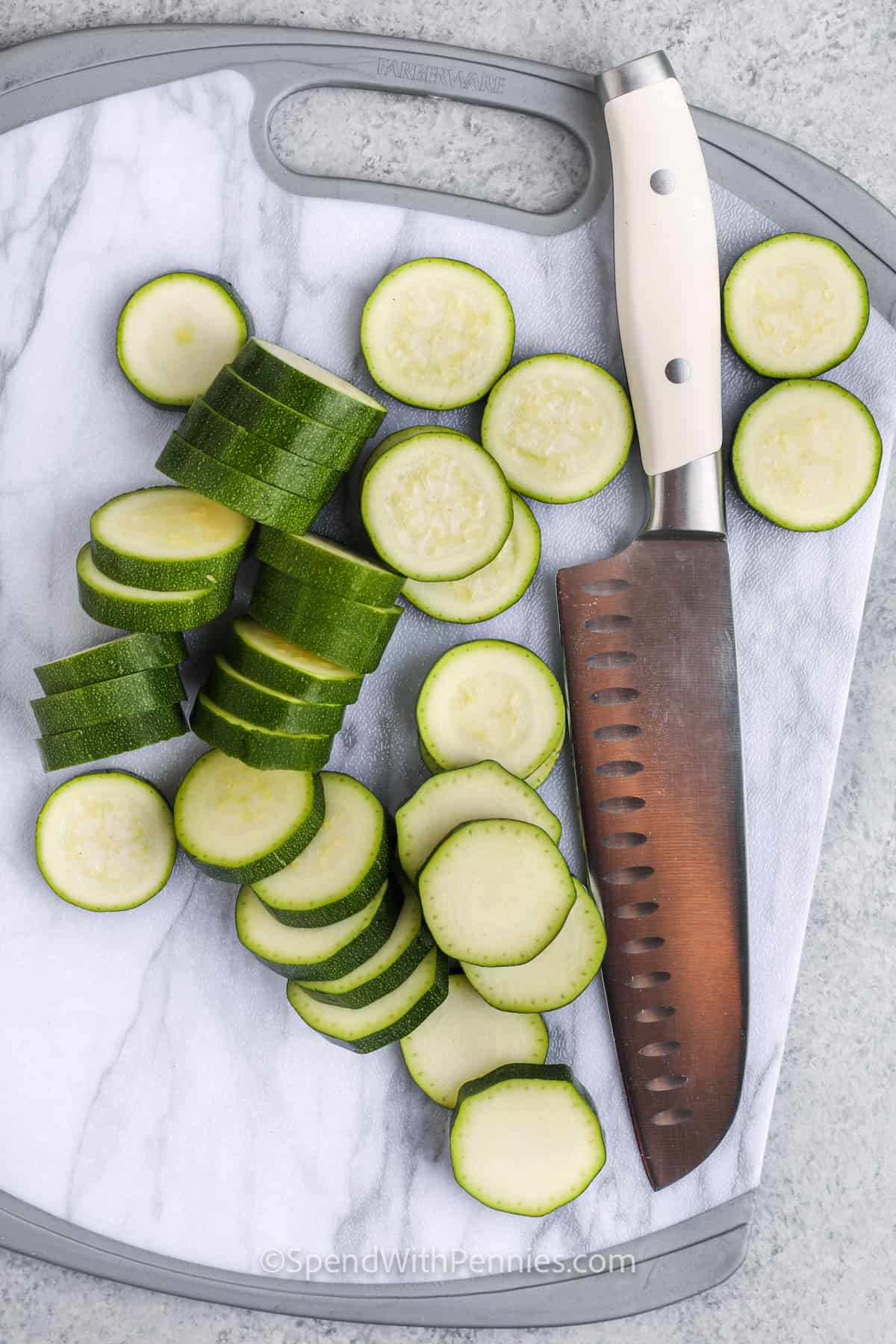 For an easy and delicious side dish, this sautéed zucchini squash recipe is just the ticket. Sliced zucchini rounds are cooked in a mix of olive oil and butter, with garlic and dried basil, until lightly browned. For a colorful variation, toss in some yellow squash. You can also add in tomatoes, onions, mushrooms, or peppers. Serve with a sprinkle of parmesan for a heartier option. It’s a quick, flavorful side that pairs with almost any dish! #spendwithpennies cutting slices of zucchini to make Sauteed Zucchini