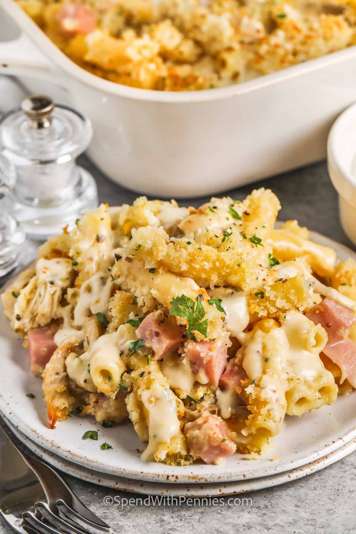 No need to make stuffed chicken, this easy chicken cordon blue casserole is simple to make and tastes just as delish! It's made with pasta in a cheesy cream sauce, and it's simple to make it into a keto or low carb recipe if desired, just leave out the pasta and Panko breadcrumbs, and sub cauliflower rice. #chickencordonbluecasserole #easyrecipe #withpasta #spendwithpennies Chicken Cordon Bleu Casserole on a plate and a dish full in the back